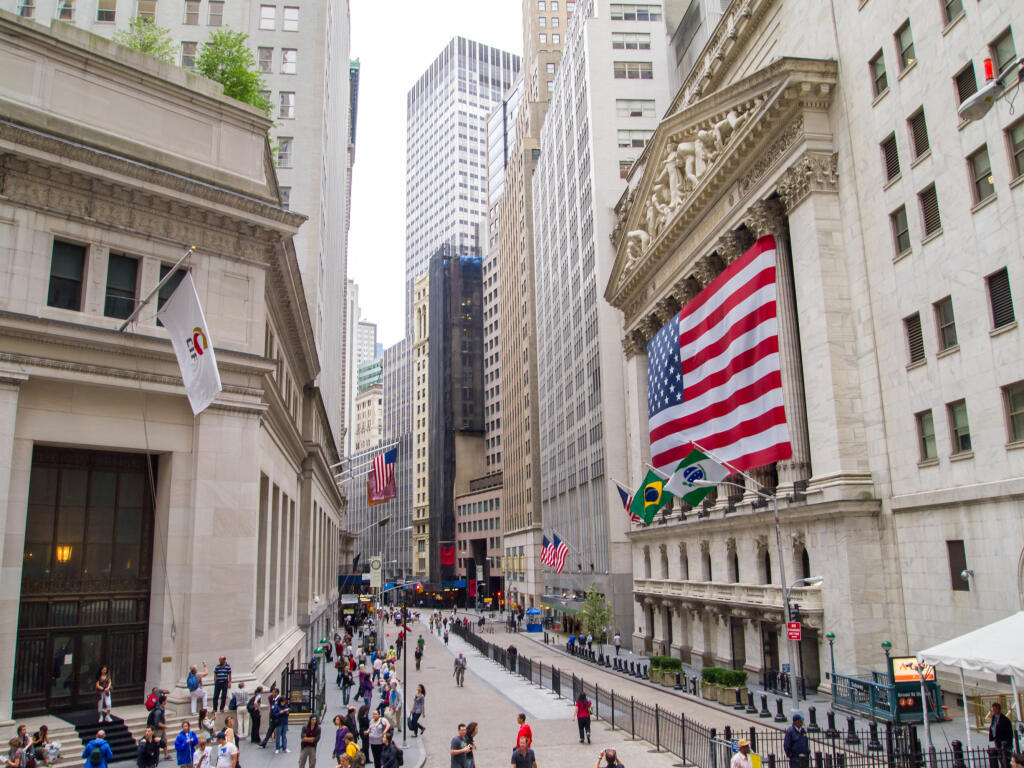 Turisti kráčajúci okolo newyorskej burzy cenných papierov zahalenej americkou vlajkou.
