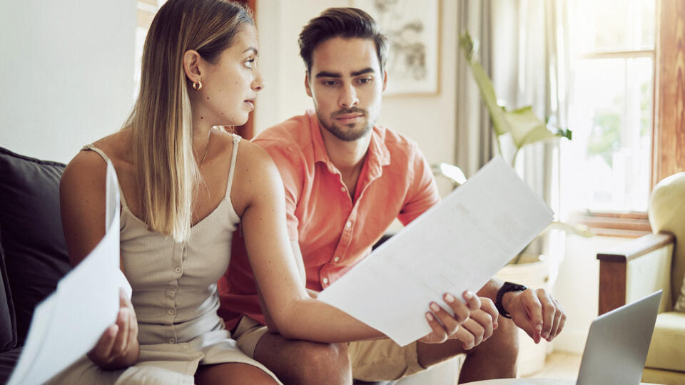 Unhappy, stressed and upset couple paying bills or debt online on with a laptop at home getting angry, planning budget. Young man and woman having a dispute over finance, savings and increasing tax