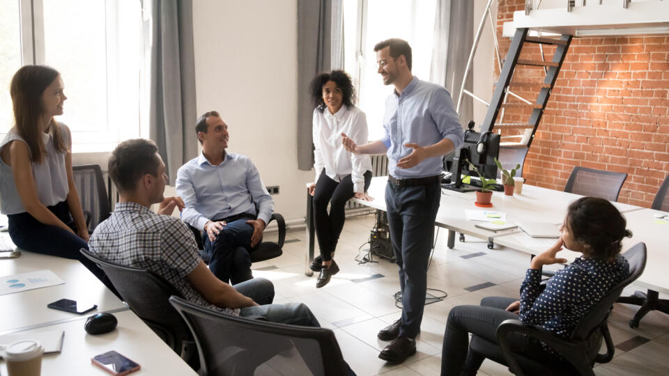 Confident male leader, coach talking with multiracial group of office workers, having good conversation with subordinate, brainstorming, discussing business strategy, ideas, team building activity