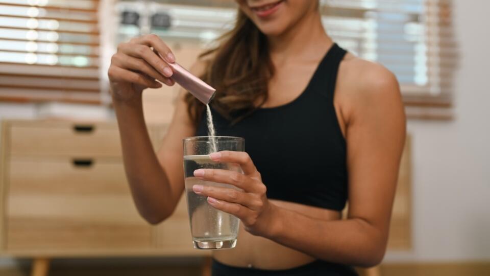 Young,Woman,Dissolving,Collagen,Powder,In,Glass,Of,Water,,Preparing