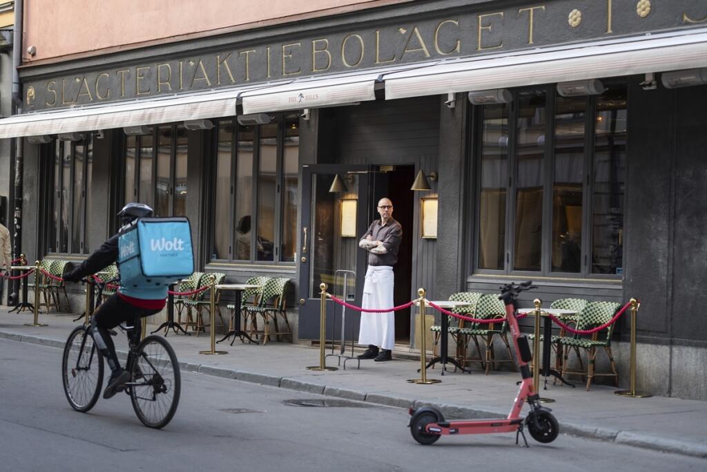 A waiter looks out from a restaurant while a food delivery person passes by on a bicycle, during the coronavirus outbreak, in Stockholm, Sweden Friday, April 17, 2020. (Stina Stjernkvist/TT News Agency via AP)