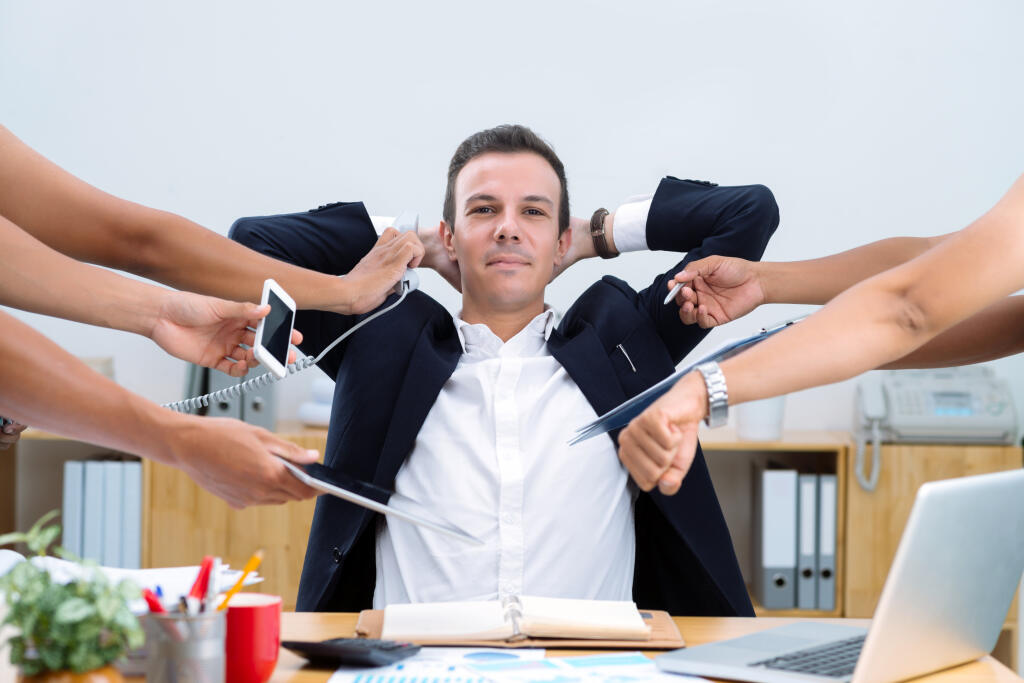 Smiling confident businessman sitting at desk and doing many tasks at once