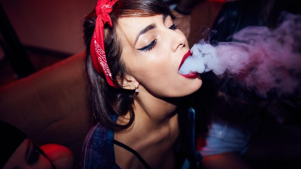 High angle shot of sexy pin up style young woman letting thick cloud of vape smoke out of mouth at nightclub party