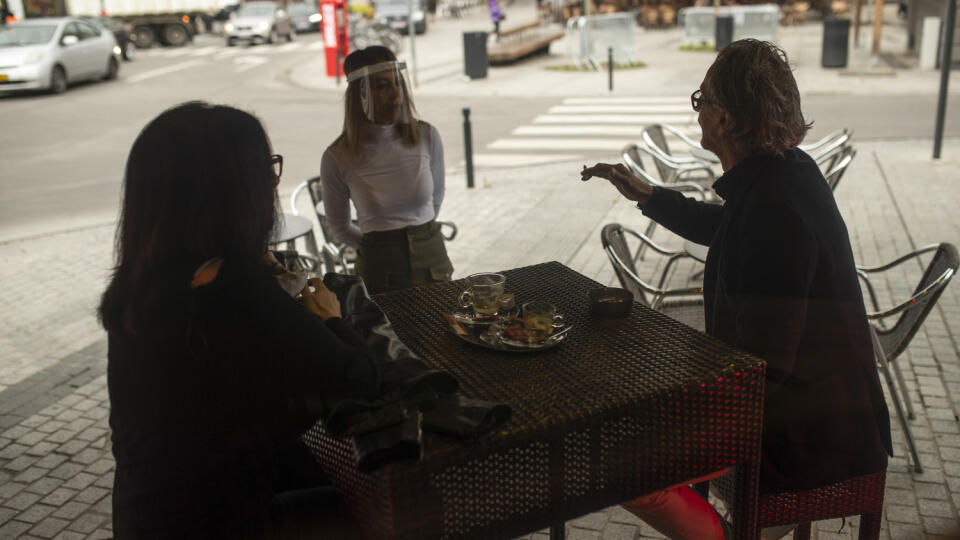 Na snímke sa zákazníci rozprávajú s čašníčkou, ktorá má na tvári ochranný štít na terase podniku v belgickom Bruseli.