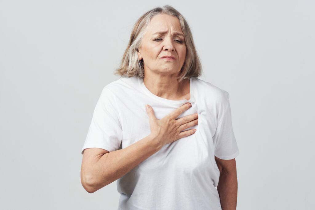Ill,Elderly,Woman,Holding,Her,Chest,Against,A,Gray,Background