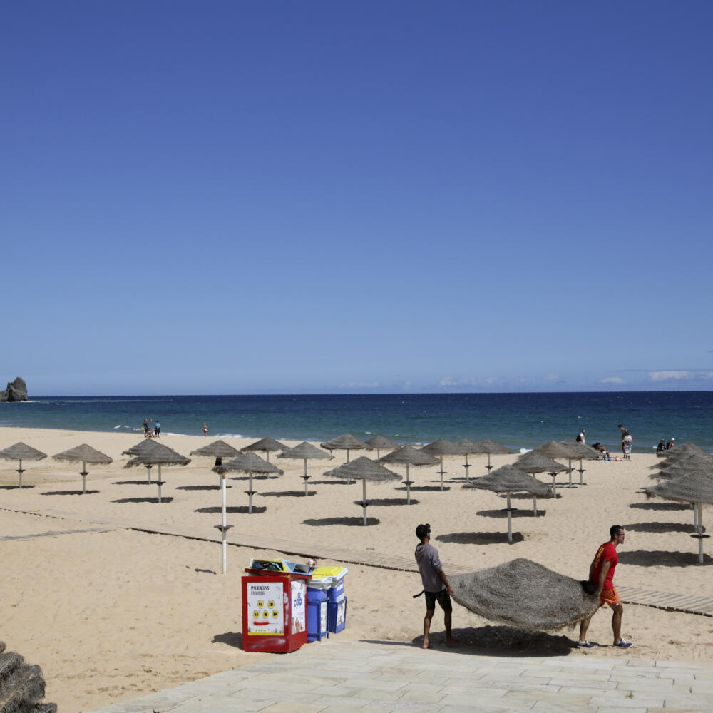 Muži rozkladajú slnečníky na pláži v portugalskom Praia da Luz 4. júna 2020.