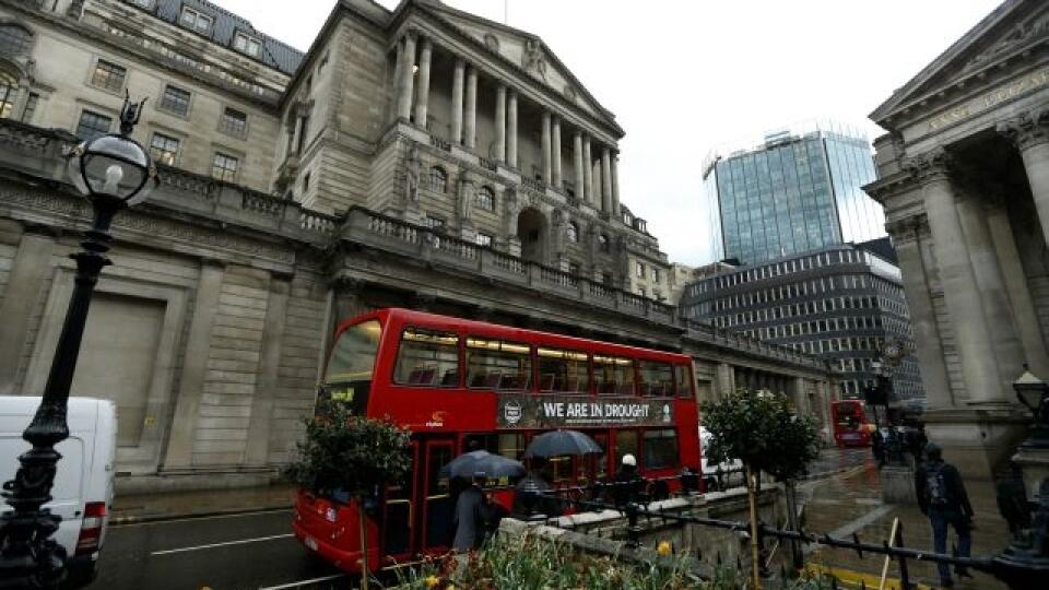People sheltering from rain under umbrellas walk past a double-decker bus bearing an advert from the Thames Water company stating