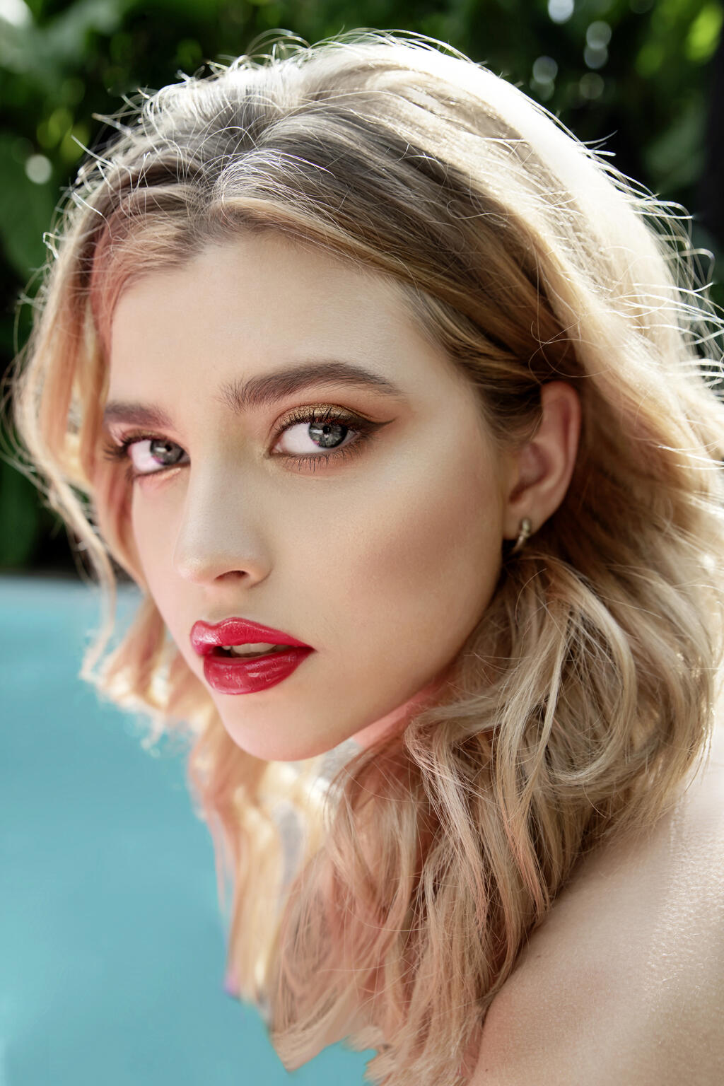 Beautiful young woman’s face with clean perfect skin front of tropical green leaves and pool water. Fashion summer portrait of model girl. Women and nature. SPA skincare and wellness. Selective focus