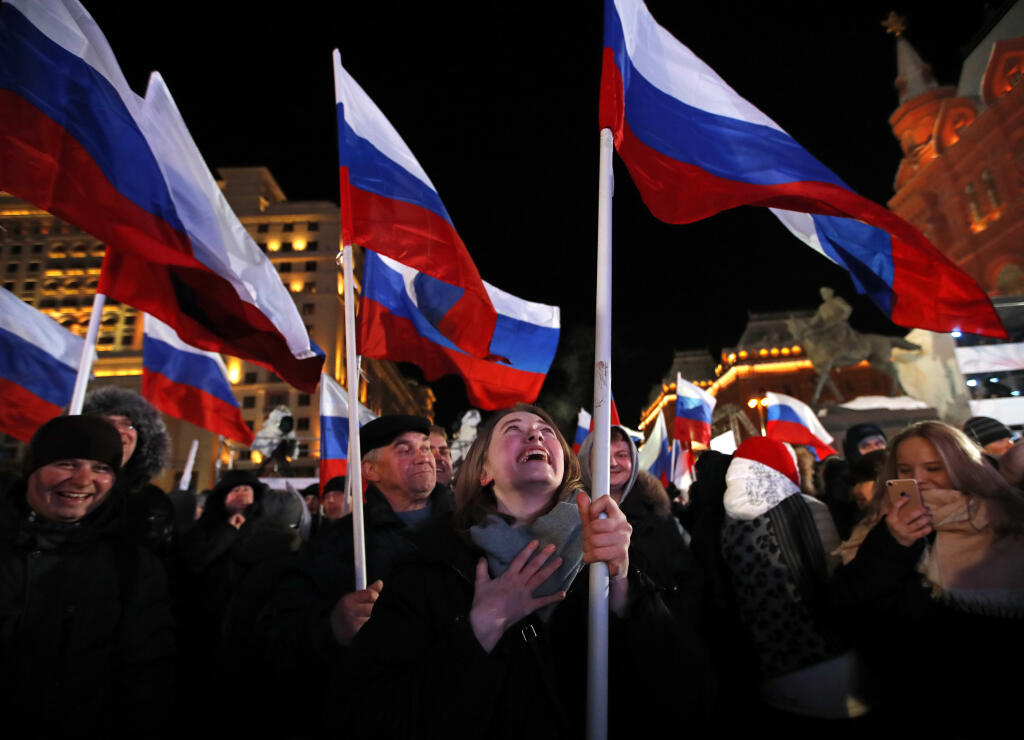 People wave Russian flags as they wait for election results in Manezhnaya square, near Kremlin in Moscow, Sunday, March 18, 2018. Russians are voting in a presidential election in which Vladimir Putin is seeking a fourth term in the Kremlin. (AP Photo/Pavel Golovkin)